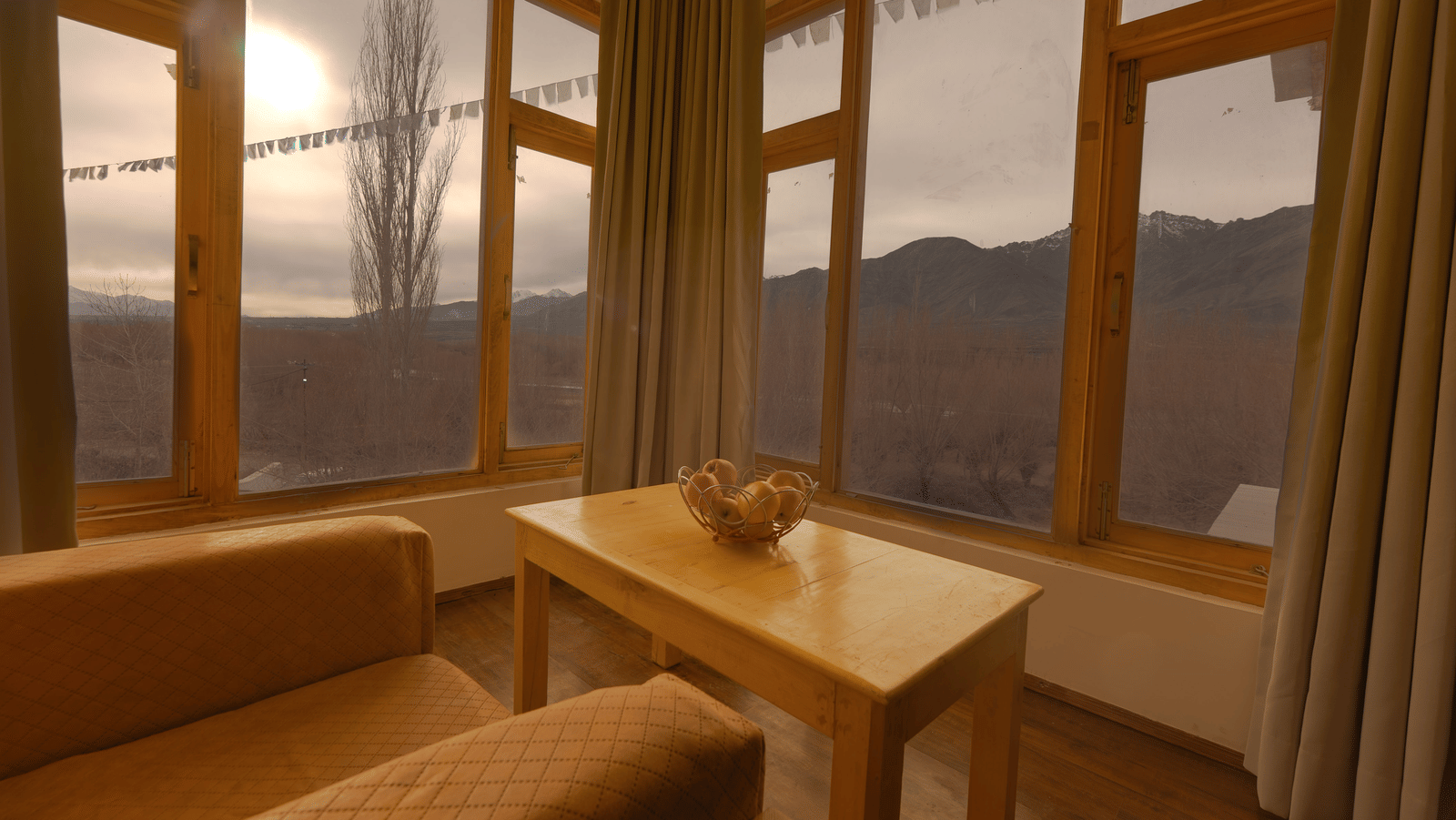 A view from a comfortable indoor seating area looking out through large windows towards the mountains at Indus Serenity Retreat.