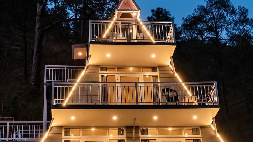 A front view of an illuminated A-frame building at dusk, with lights glowing from within and around it.