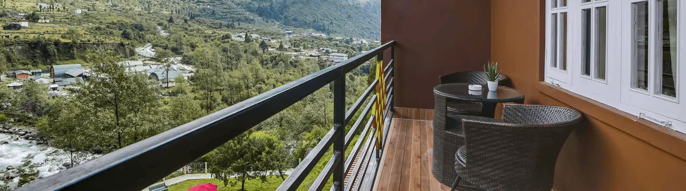 A balcony at the Orsino Khangri Karpo Retreat & Spa, Lachung with a table, chairs, and a view of mountains and a valley.