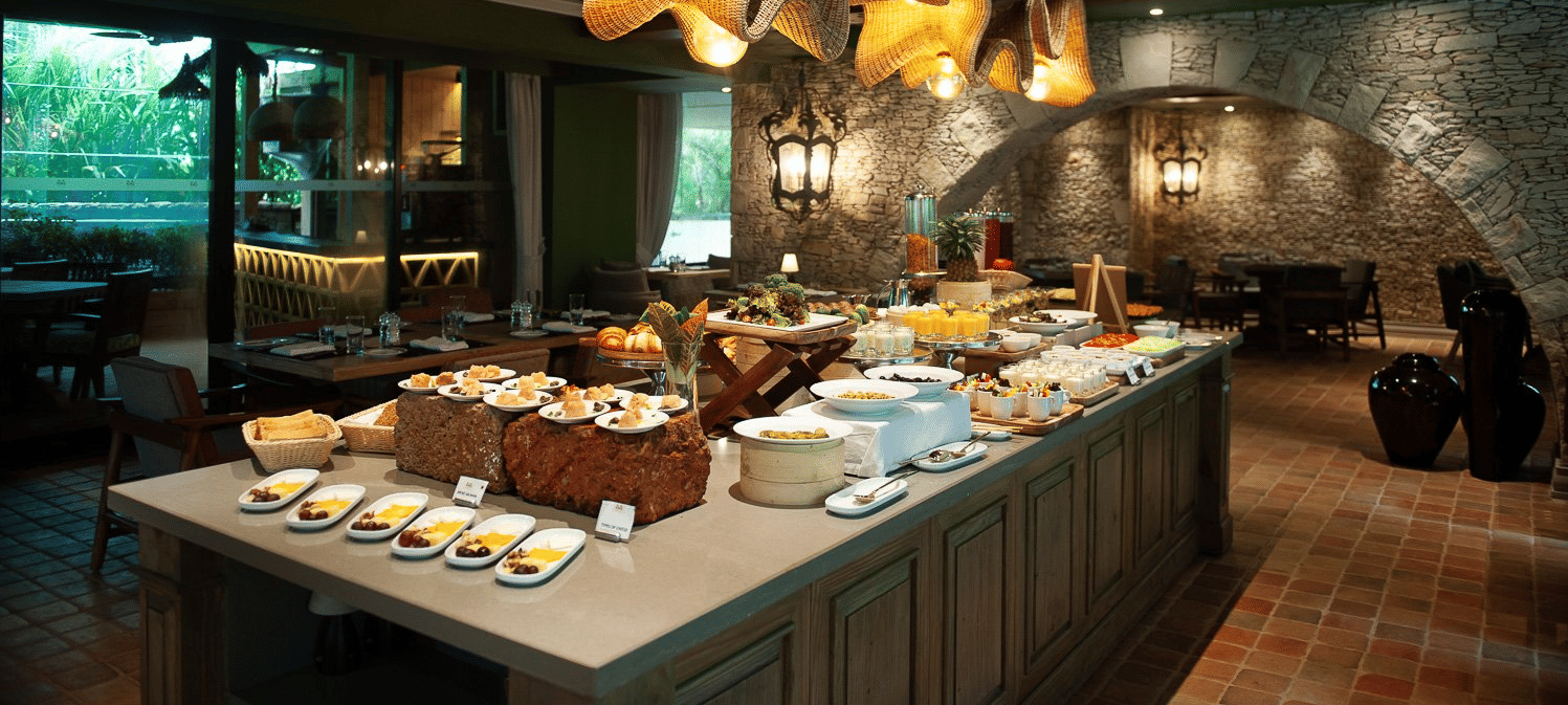 A lavish breakfast buffet spread at the Mila Restaurant at The Evren, Vagator, featuring a variety of dishes on display under the woven light fixtures.