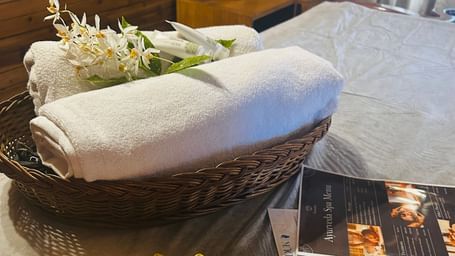 A wicker basket with rolled towels and flowers next to a gold tray with a candle, red petals, and toiletries at Cedar Inn, Darjeeling.