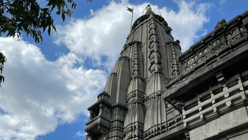 A stone temple structure with carved walls and a tall spire rising above the building against a blue sky.