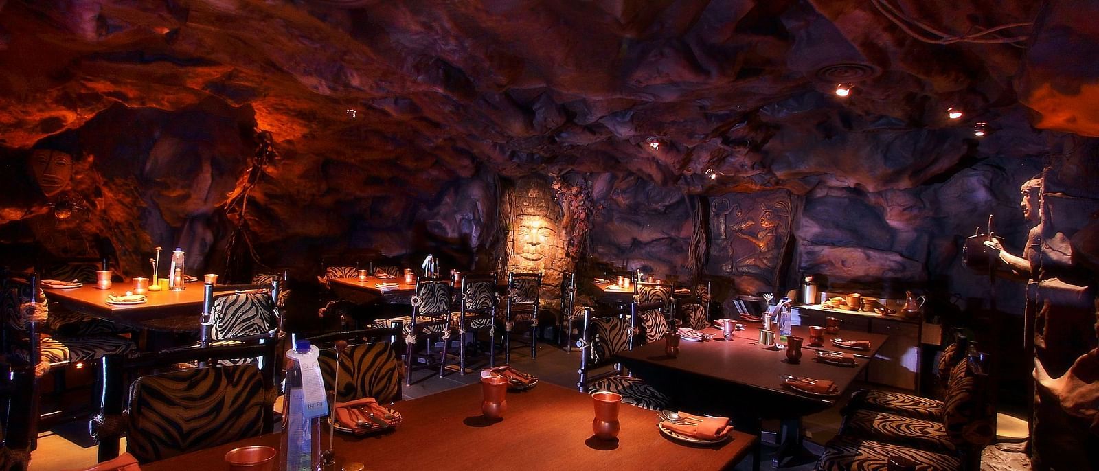 An image of cave themed restaurant with a few sets of chairs and table - The President Hotel Jayanagar Bangalore
