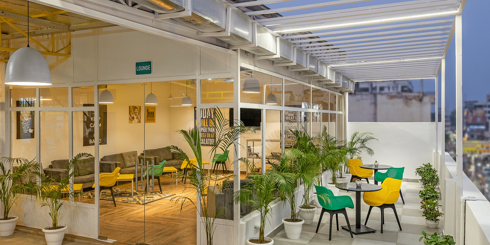 An image of a lounge featuring both indoor and outdoor seating,  with a few plants outside, beautifully lit for the evening atmosphere.