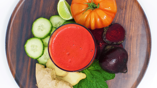 a wooden plate with a glass of red juice surrounded by fresh cucumber, tomato, beetroot, ginger, lime, and mint leaves at YO1 Longevity & Health Resorts