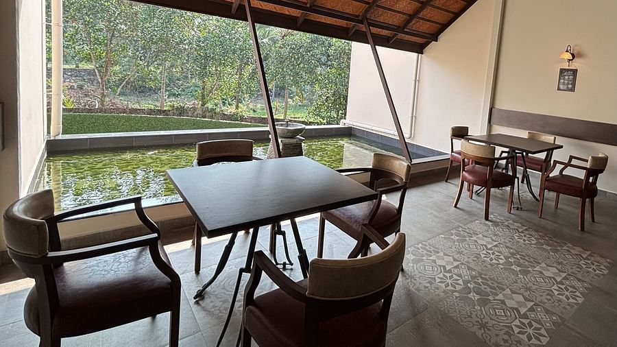 Dining area with several wooden tables and chairs, and a partial view of the roof with brown tiles at Bistro Cafe. - Still Waters, Varkala