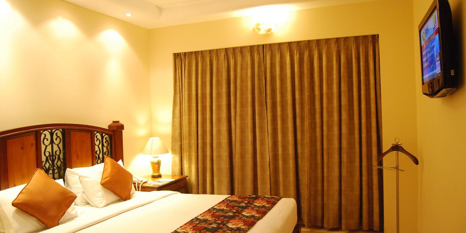 A king bed with a large mattress and cushions, facing a flatscreen TV in a well lit room