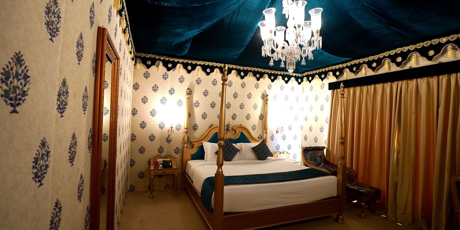 Image of a room with a bed, a mirror on the side and a chandelier hanging from the ceiling.