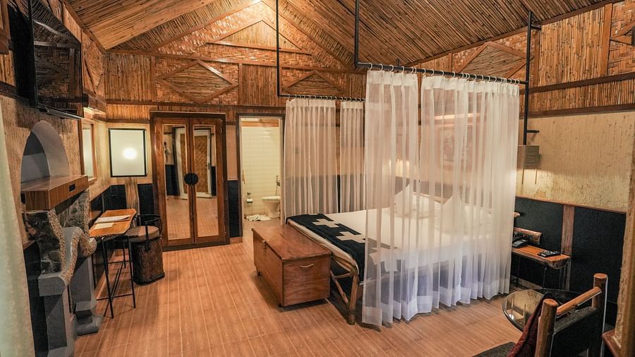 A bedroom with a bed, a curtain, and warm lighting, wooden interior - The Den Corbett Resort & Spa, Kumeria.