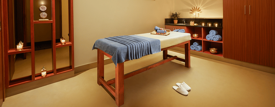 Spa room with a massage table, folded cloth, red partition, and storage cabinets - Karur 