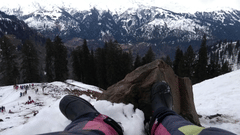 Person Wearing Black Boots and sitting in a Snowy Mountain watching a snow-capped mountain.