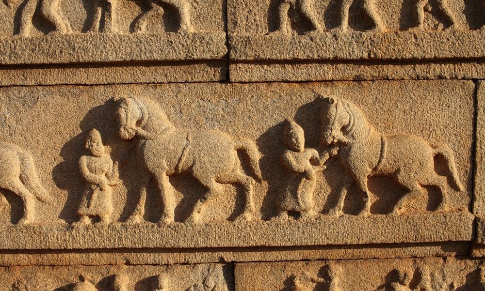 Stone carving of men with horses on a temple wall.