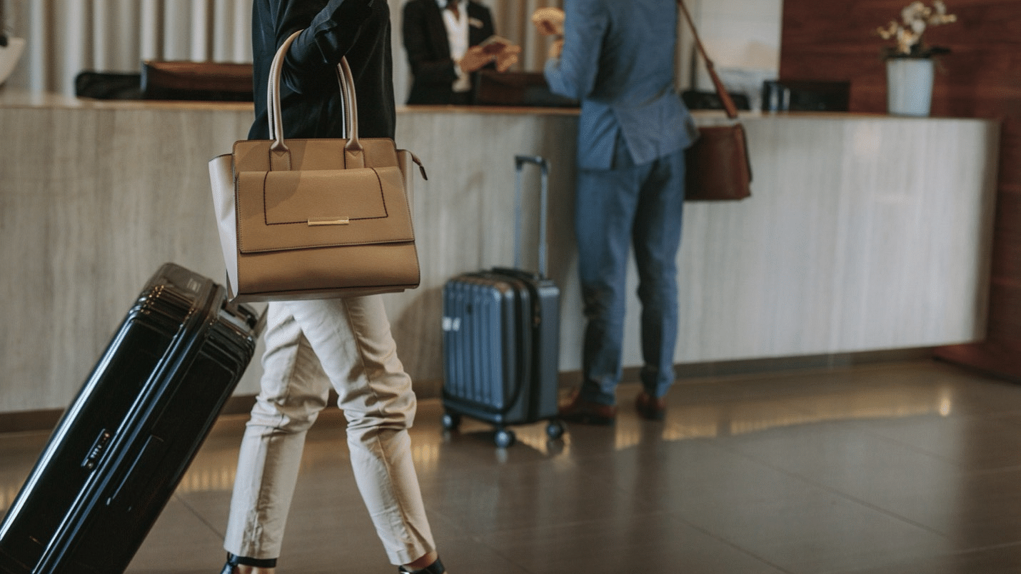 Hotel check-in with a person in a suit, luggage on a trolley, reception desk in the background.