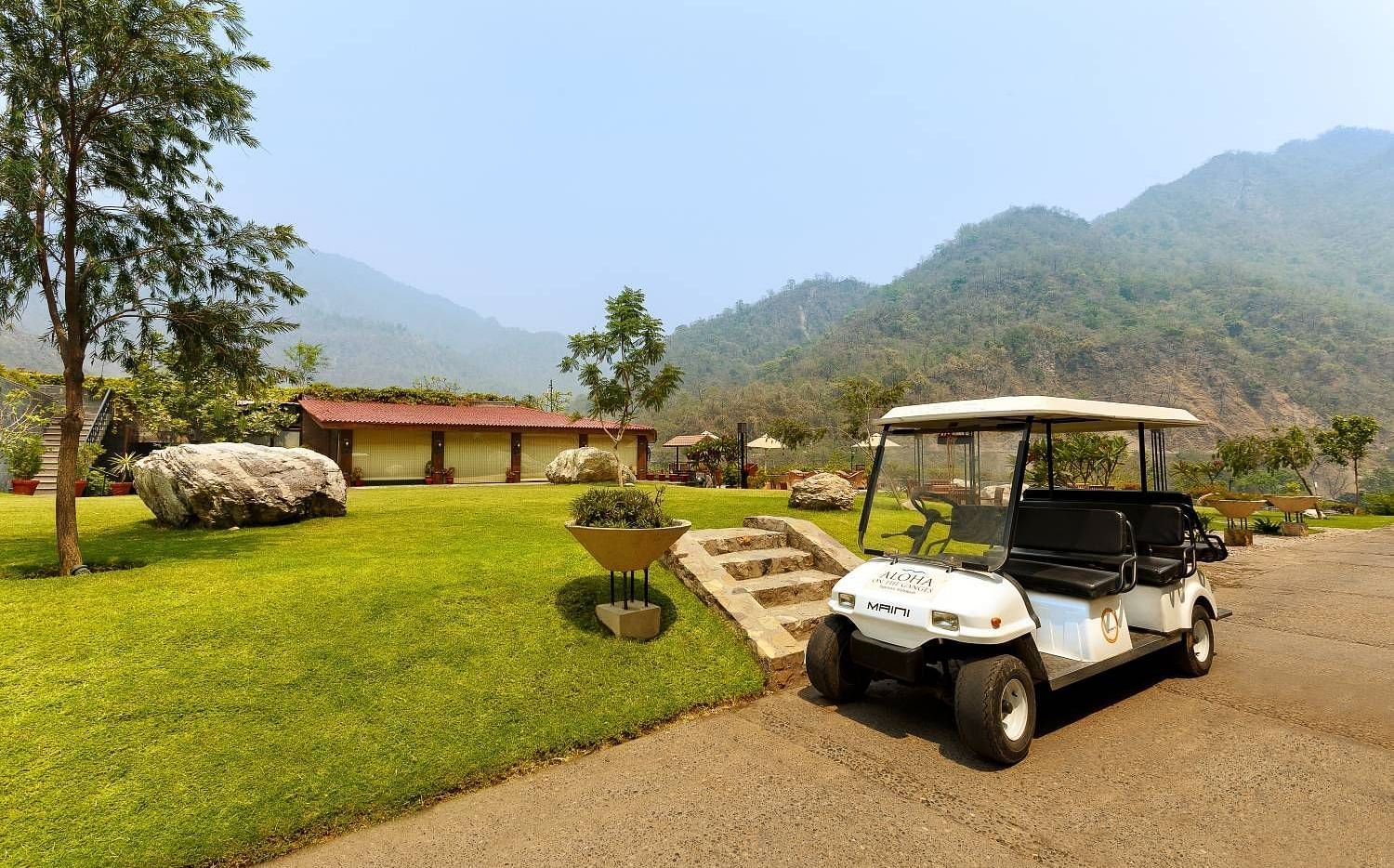 A golf cart parked on a gravel path in a lush landscape in the background and mountains in the distance.