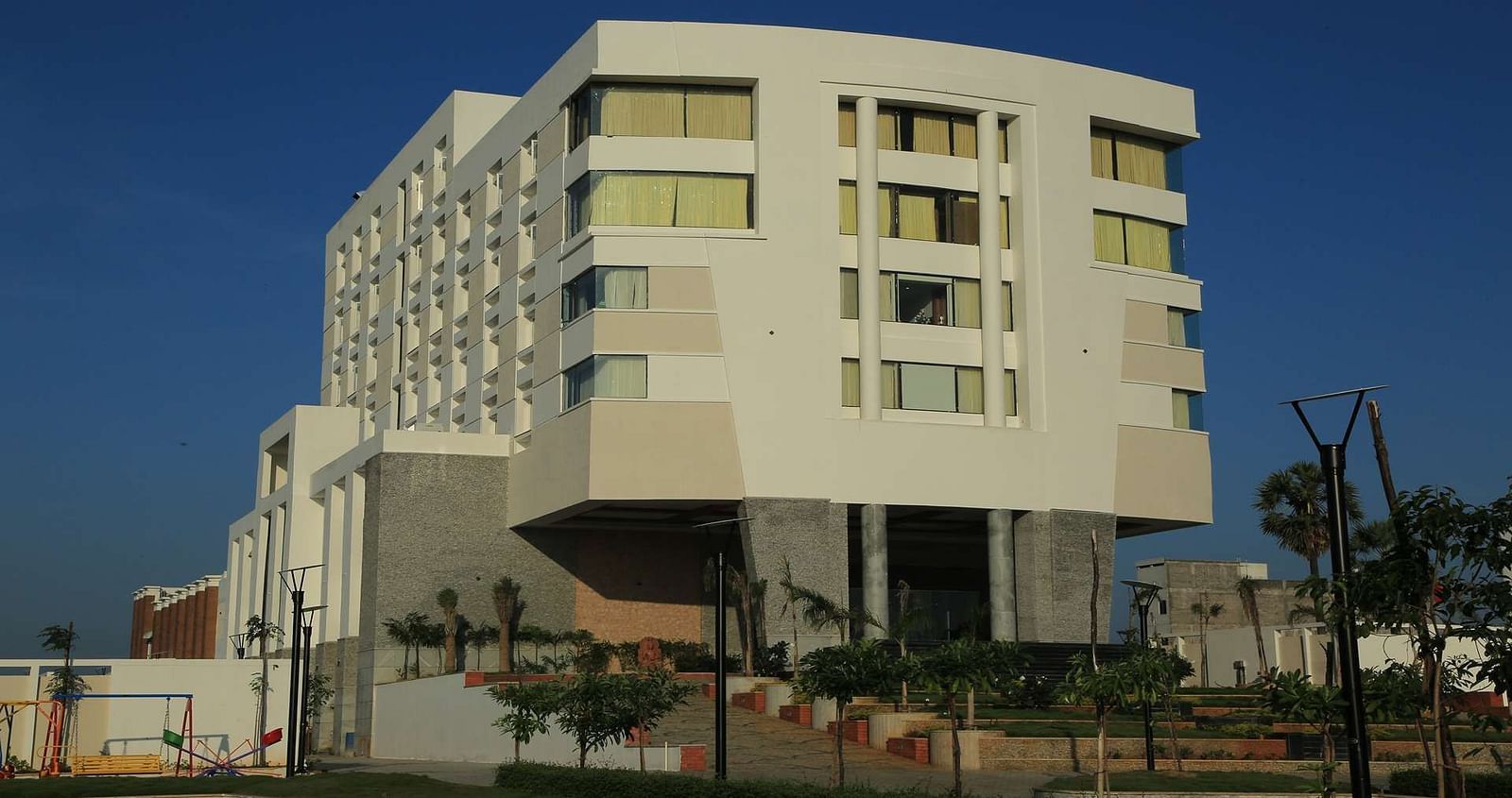 A modern white multi-storey hotel building against a blue sky, offering a luxurious stay in a prime location.- Dhanalakshmi Srinivasan Hotels, Perambalur