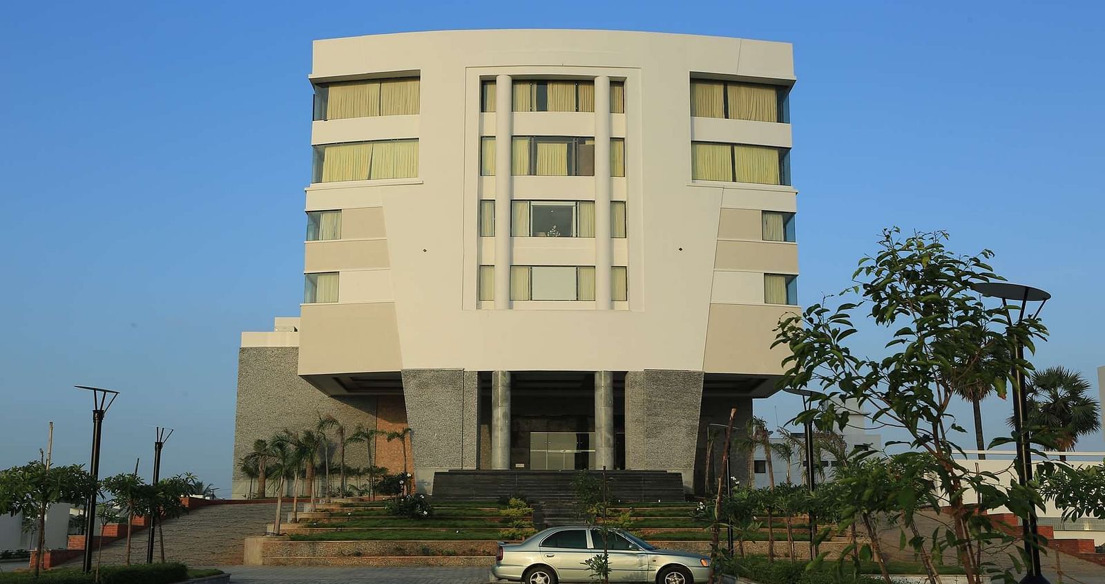 Front view of facade of Dhanalaksmi Srinivasan Hotels, Perambanur  with a backdrop of clear blue sky.
