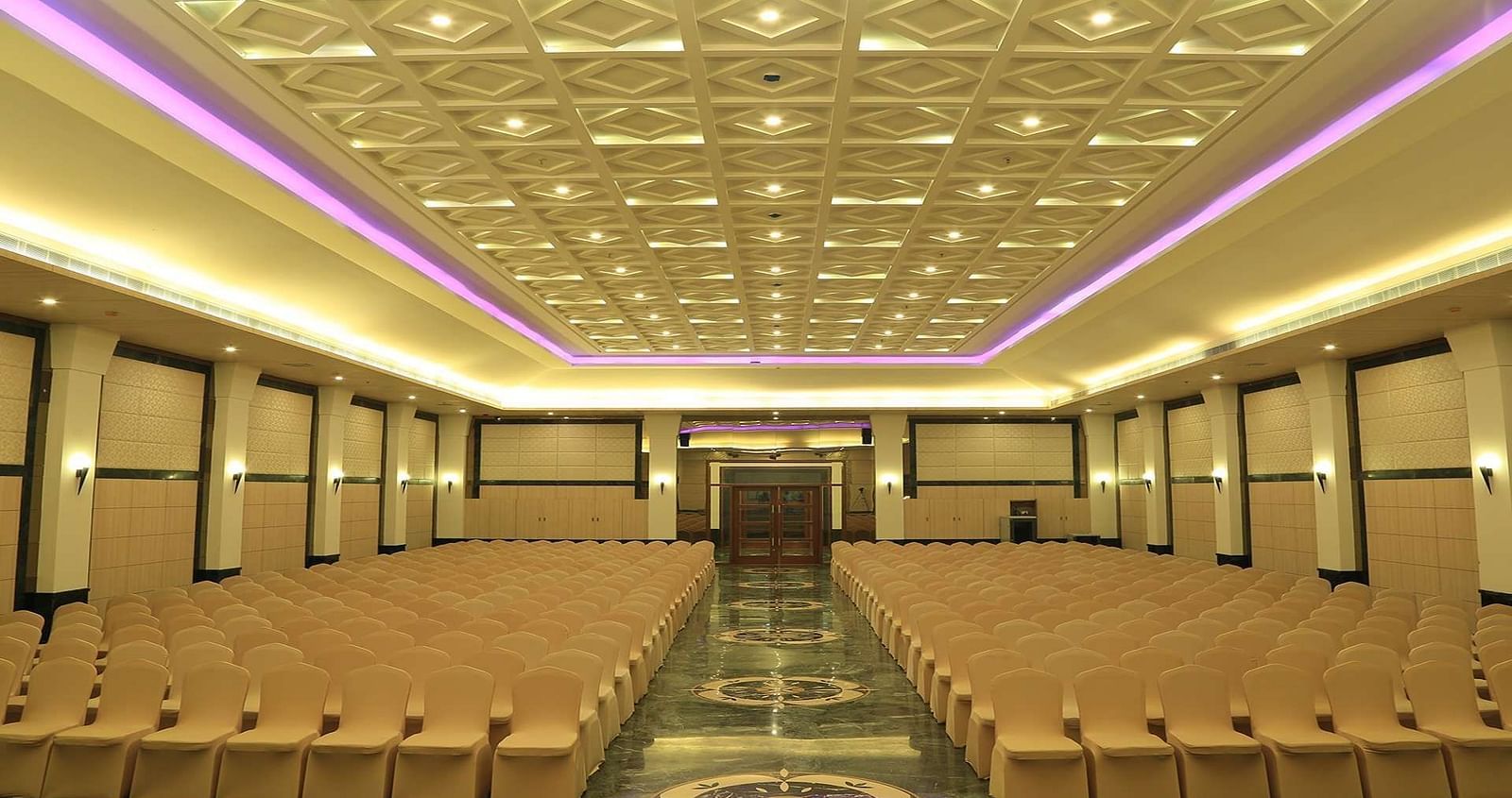 Over view of DS Mahal Hall at Dhanalakshmi Srinivasan Hotels, Perambalur with  chairs arranged in theatre seating and chandelier on top. 
