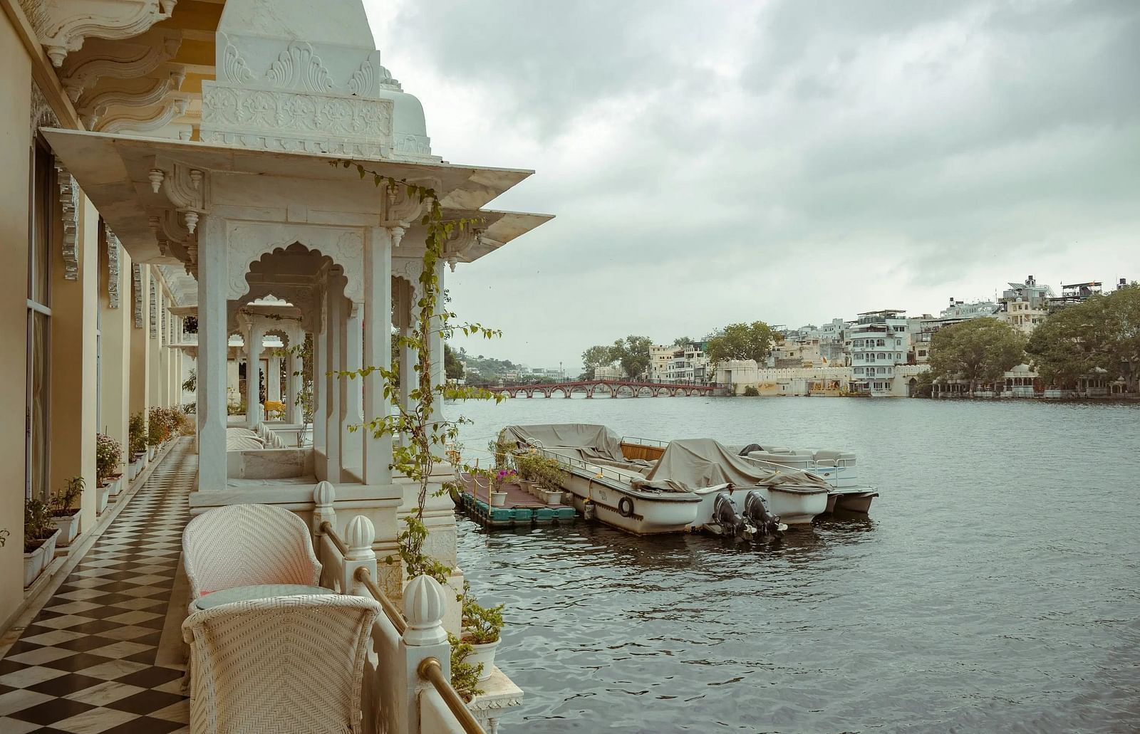 View from a balcony overlooking Lake Pichola in Udaipur, India, with boats docked and a bridge in the distance.