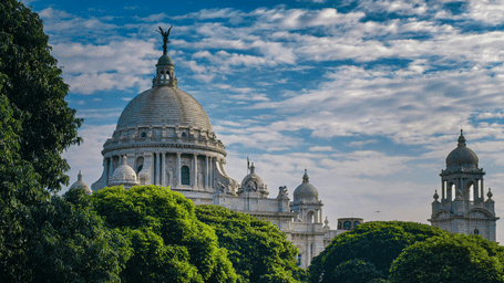 The Victoria Memorial, a grand white marble building,  surrounded by green trees and a blue sky in Kolkata.