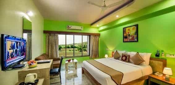 A brightly coloured room with a double bed, a television, and a balcony - Lion Lords Inn Rajula