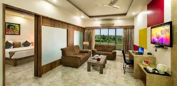 A spacious room including a seating area with sofas, a television, and large windows - Lion Lords Inn Rajula