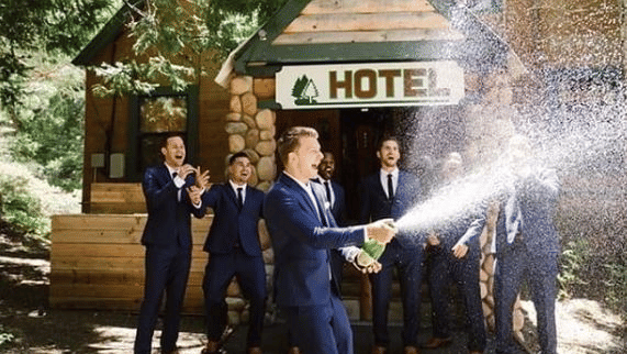 Wedding guests celebrating outside a rustic hotel entrance with a champagne spray during an outdoor event at Shaver Lake Village Hotel.