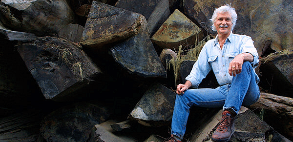 An image of an old man sitting on the rocks and smiling at the camera