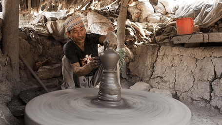 An elderly Newar artisan crafting a clay vessel on a large spinning potter's wheel in a Bhaktapur workshop, Nepal.