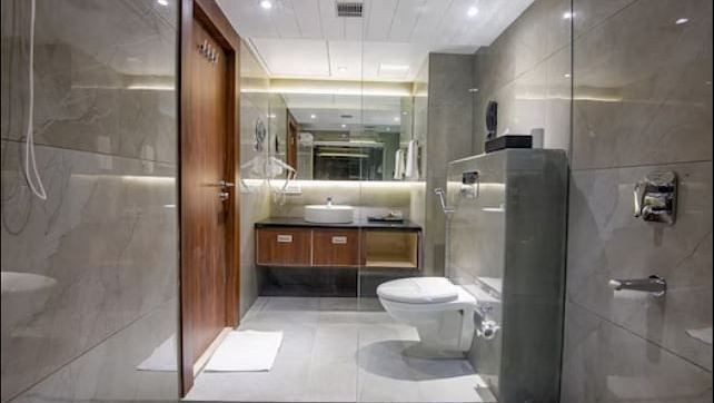 A luxurious washroom with modern fixtures, including a glass shower enclosure, a large mirror, and  grey tiled walls at Yashshree The Imperial Inn, Siliguri.