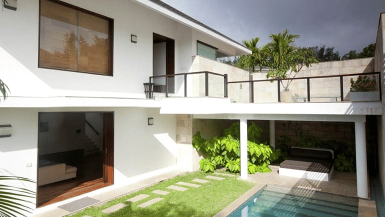 Exterior view of The Estate Terrace Villas in Chikmagalur with shrubs, two floored building, a plunge pool, trees, a small lawn area and dark could in the background seen.