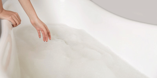 A person's hand dipping into the water in a bathtub at YO1 Longevity & Health Resorts