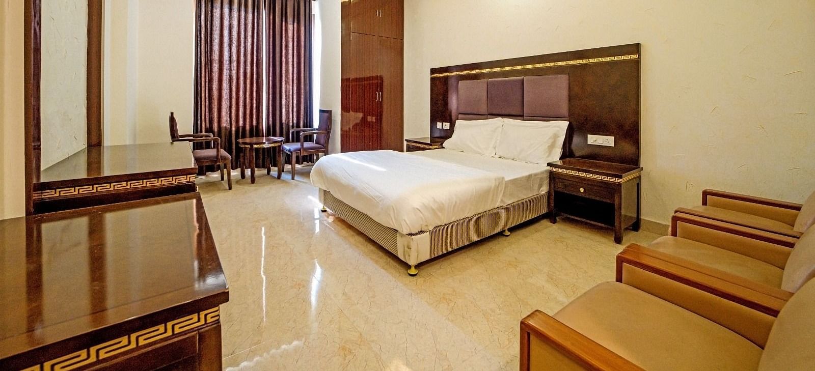 Elegant bedroom at Grassfield Riveria Resort, Jaipur, featuring a large bed, wooden furniture, and warm ambient lighting.