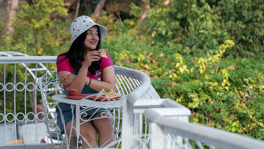 A woman enjoying the serene view from a white wrought-iron balcony at Maati Resort By The Lake Hill, Jeolikote.