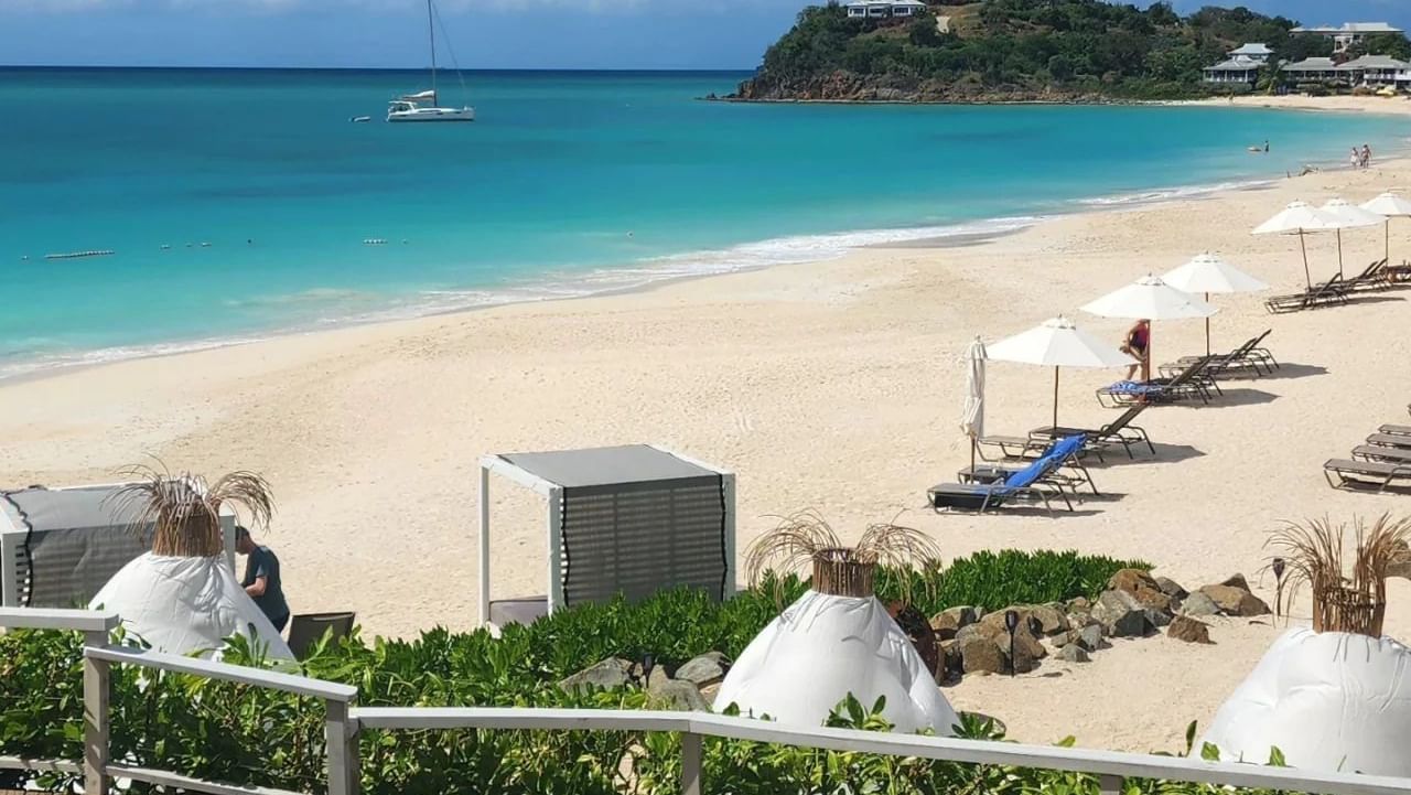 A beautiful white sand beach with turquoise water, lounge chairs, and umbrellas viewed from a patio.