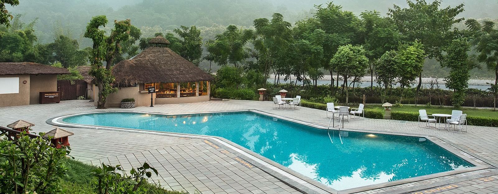 An image of a swimming pool surrounded by trees and huts