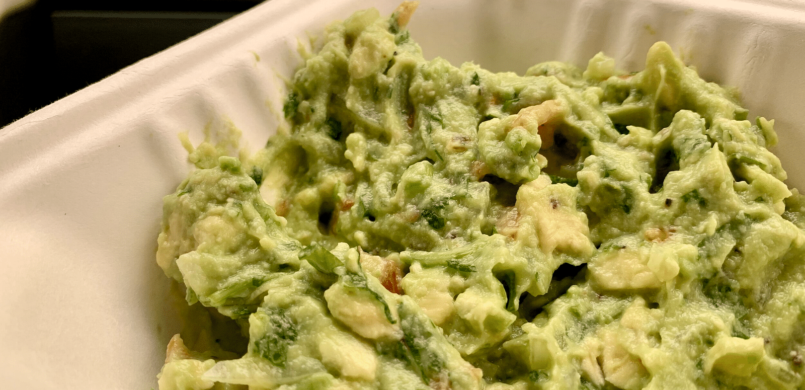 A close-up view shows a bowl of chunky guacamole with visible pieces of avocado, tomato, and cilantro.