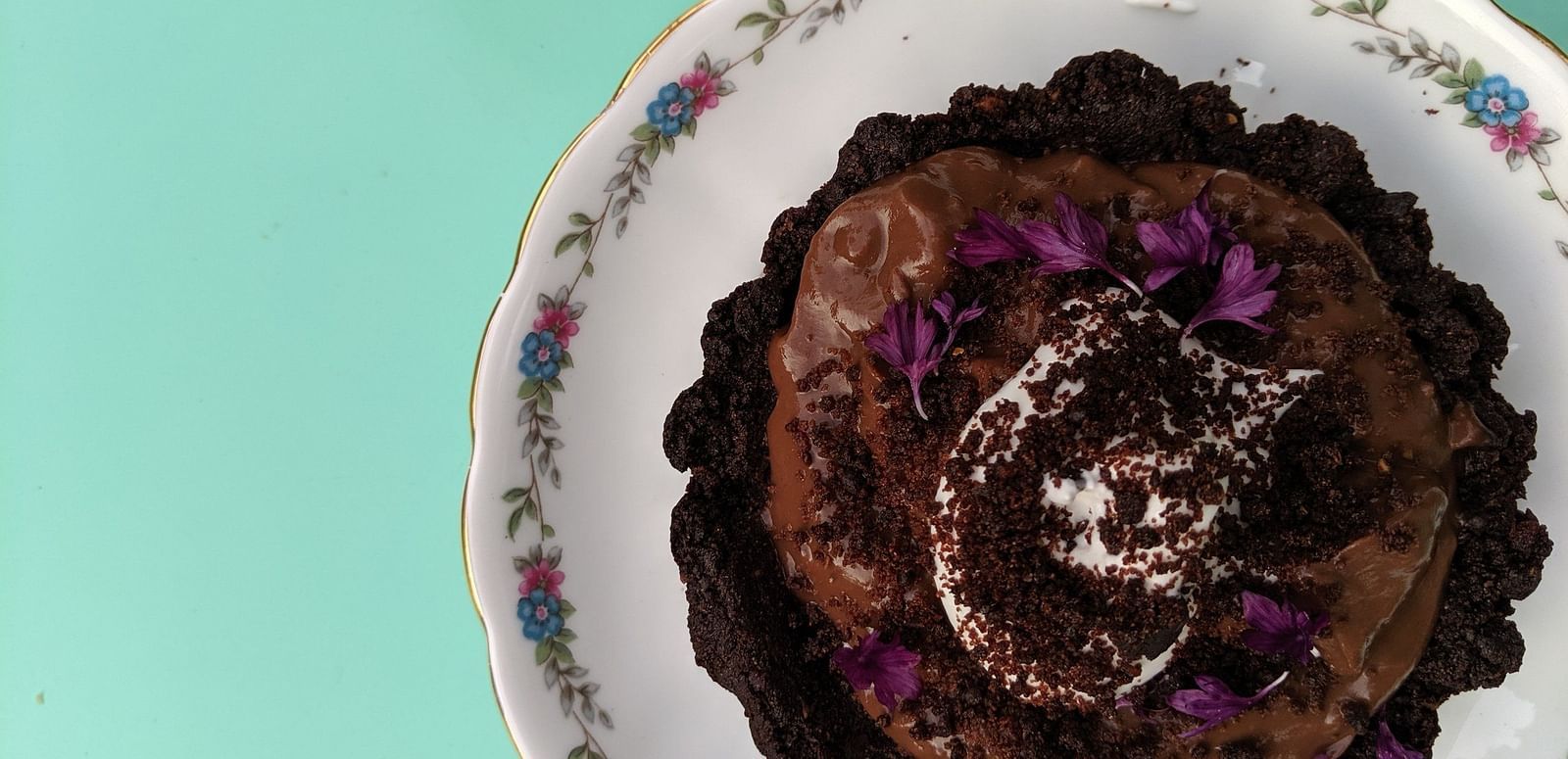  A small, round dessert with a dark base and a creamy topping is presented on a decorative plate, viewed from above.