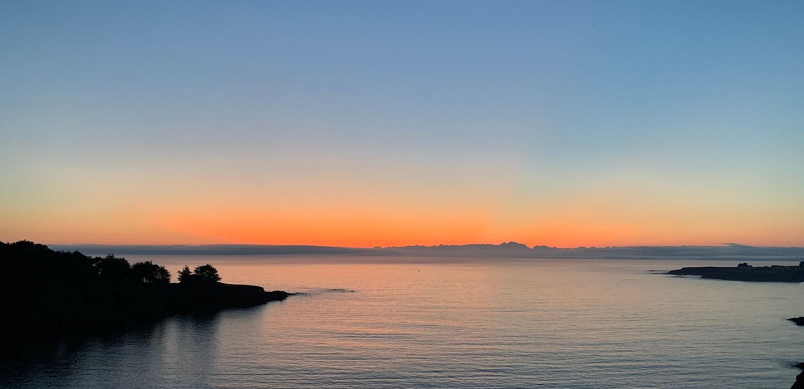 A twilight scene with a gradient sky above a dark silhouette of a rocky coastline meeting the ocean.