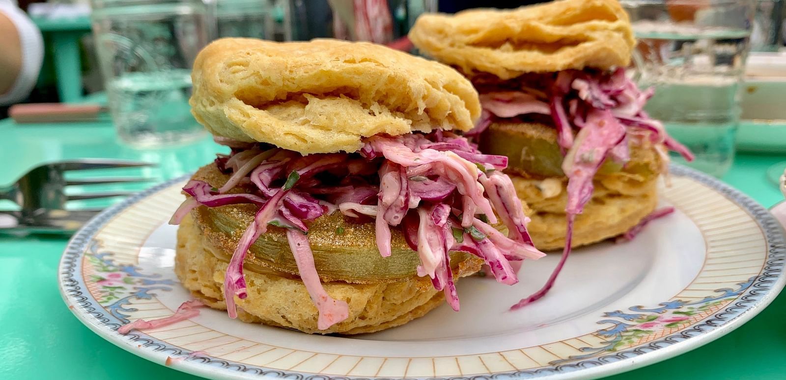 Two biscuit sandwiches with filling and shredded topping are served on a plate, with glasses and a fork visible in the background.