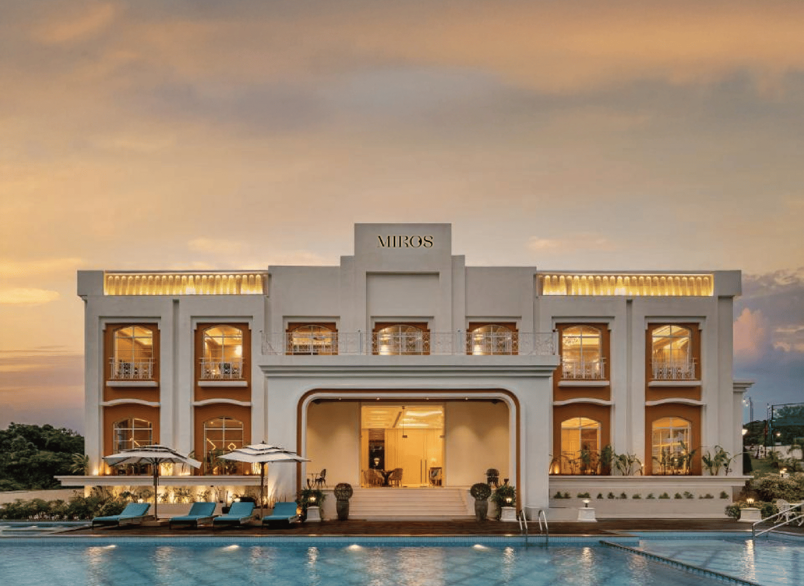 A full view facade of the best resort in Goa, MIROS Hotels with a calm swimming pool in the foreground along with beautiful sunset sky in the background.