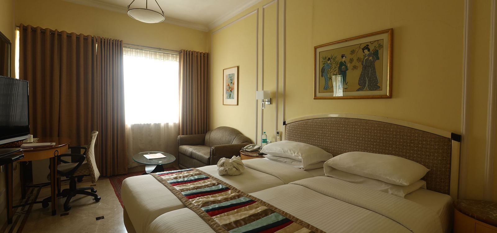 Twin beds in the Superior Room with sunlight peeking through the windows at Regency Hotel, Mumbai.