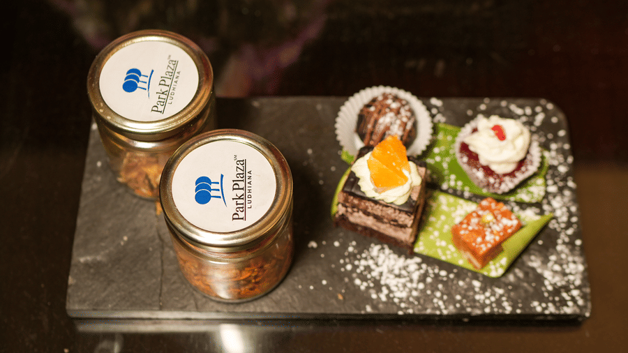 A dessert platter at Park Plaza Ludhiana featuring two branded jars and assorted petit fours including a tart and decorated bites served on a dark slate board.