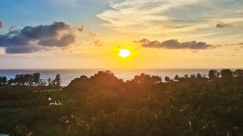 The sunrise view over the trees and beach, set against a slightly cloudy sky, offers a serene scene at Cloud9 Sarovar Premiere, Palolem Goa