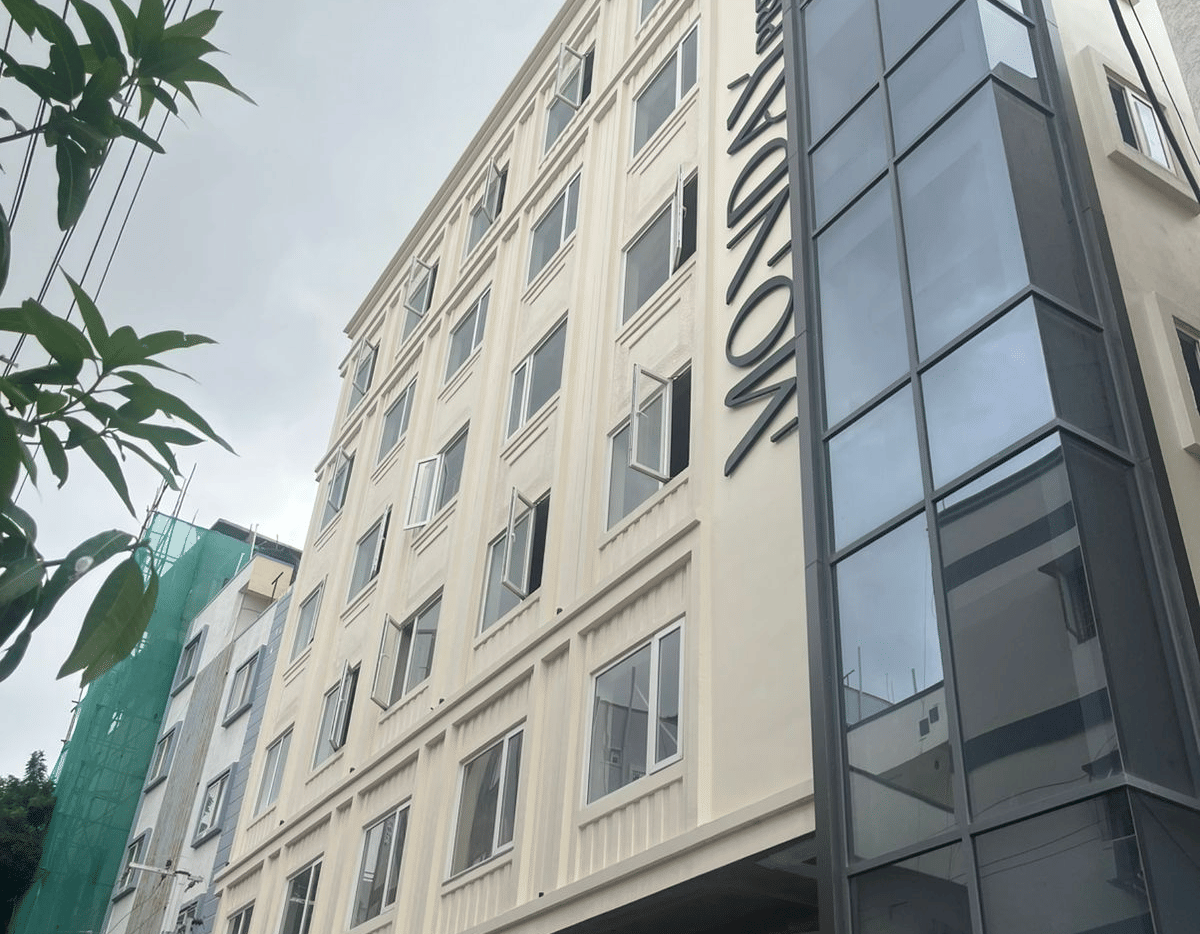  Contemporary exterior view of Monday Premium, Madhapur, showing a multi-storey building with a glass-fronted stairwell and a cream-coloured facade. 