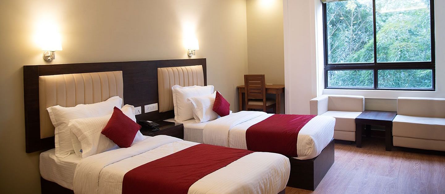 A hotel room in Gangtok featuring twin beds, warm lighting, and a window offering stunning views - Summit North Star, Gangtok
