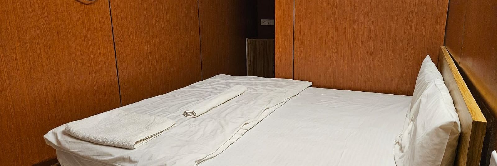 Corner view of a double bed with plain white bed sheet along with a wall mounted television at the Dream Vision Guest House.