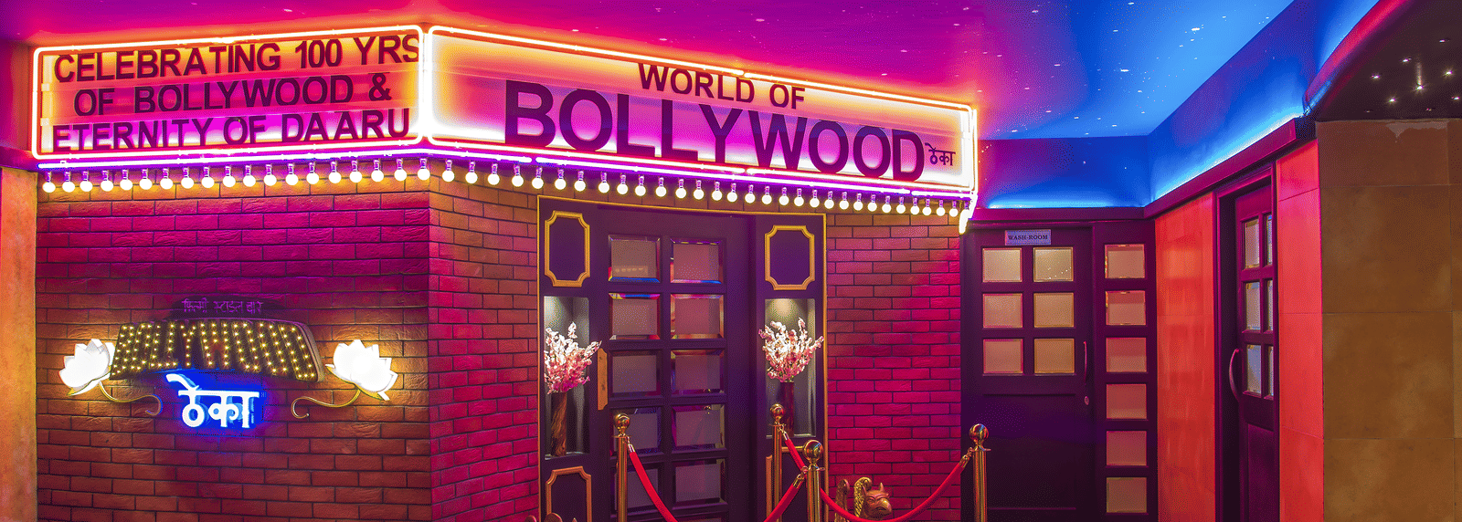 An entrance with a red carpet, ropes, neon lights and a glowing signboard reading 'BOLLYWOOD' at Infiniti Hotel, Indore.