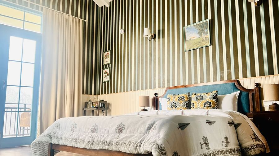 Chic hotel bedroom with striped walls, a large window, wooden floor, and a modern wooden bed with decorative pillows  | Faraway Cottages, Auli