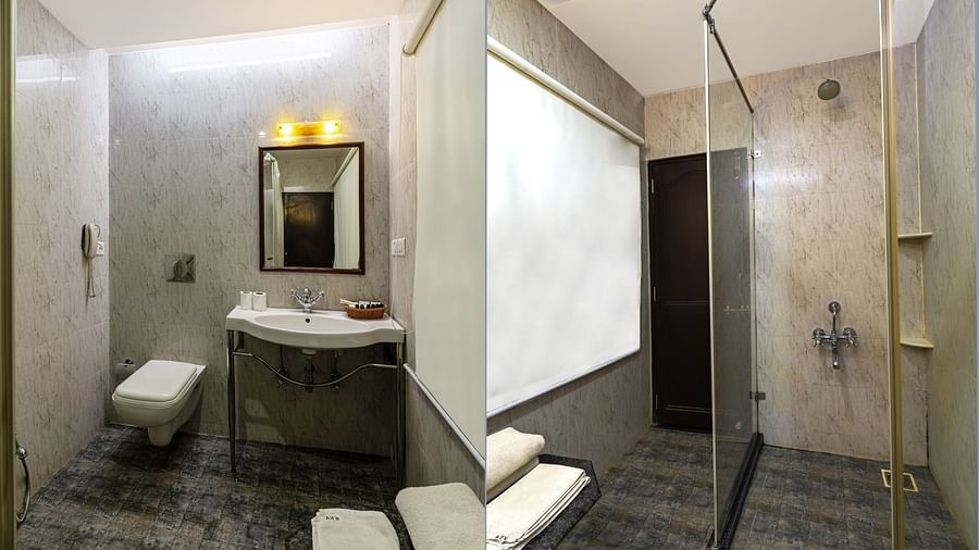 A spacious bathroom featuring a wall-mounted mirror above the washbasin, a western toilet adjacent, and a glass partition that separates the shower area | Panna Vilas Udaipur