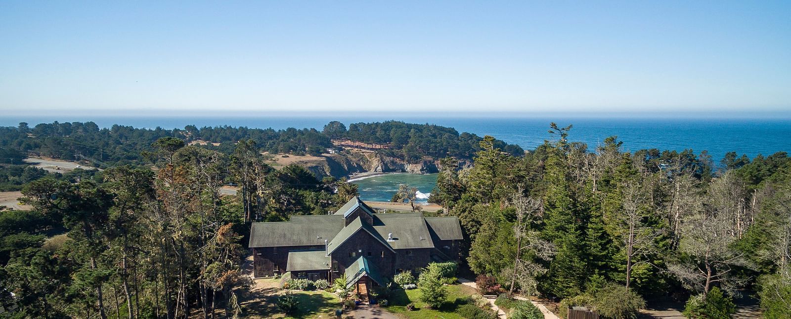 An aerial view of a hotel covered in lush green trees with the Mendocino coast in the background - Brewery Gulch Inn & Spa